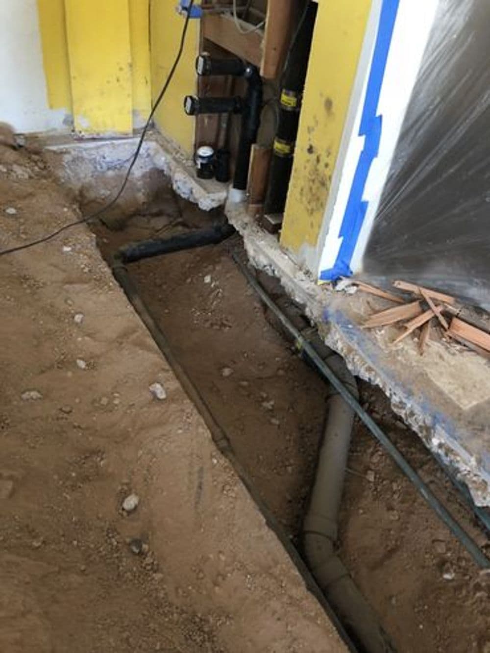 Exposed plumbing and electrical lines in a home renovation project with dirt flooring.