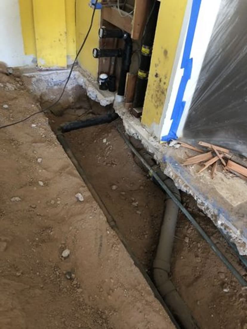 Exposed plumbing and electrical lines in a home renovation project with dirt flooring.