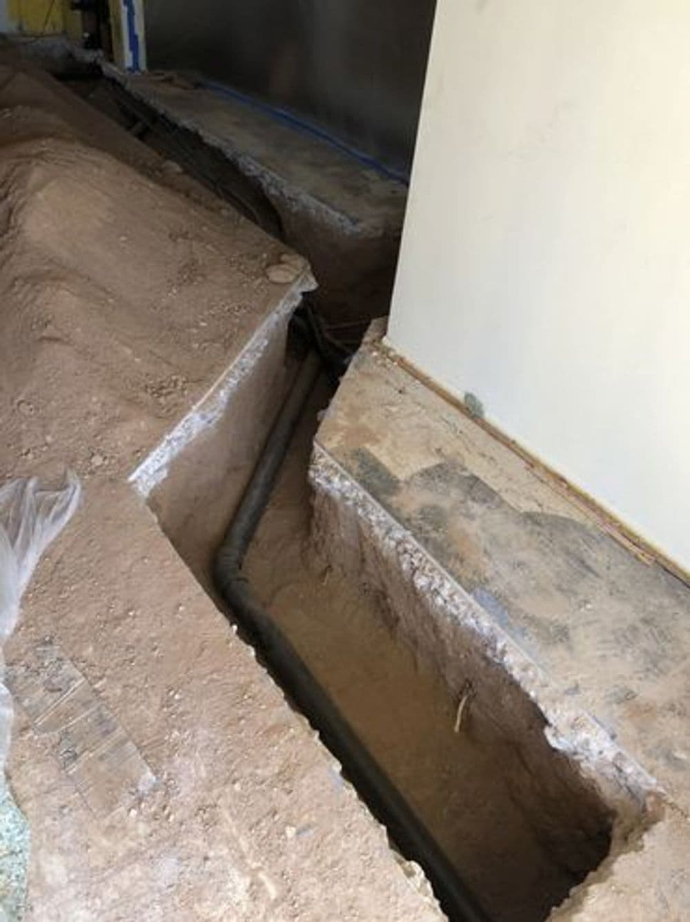 Exposed trench with plumbing pipes during home renovation process.